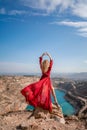 Rear view of a beautiful sensual woman in a red long dress posing on a rock high above the lake in the afternoon Royalty Free Stock Photo