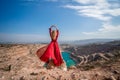 Rear view of a beautiful sensual woman in a red long dress posing on a rock high above the lake in the afternoon Royalty Free Stock Photo