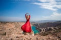 Rear view of a beautiful sensual woman in a red long dress posing on a rock high above the lake in the afternoon Royalty Free Stock Photo