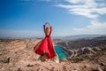 Rear view of a beautiful sensual woman in a red long dress posing on a rock high above the lake in the afternoon Royalty Free Stock Photo