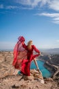 Rear view of a beautiful sensual woman in a red long dress posing on a rock high above the lake in the afternoon Royalty Free Stock Photo