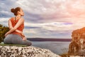 Rear view of the beautiful woman doing yoga exercises on the rock.