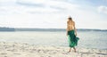 Rear view of beautiful woman in green silk walking along the sea