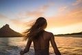 Rear view of a beautiful young woman with long hair flying in the air and enjoying the sunset on the beach, Female surfer rear Royalty Free Stock Photo