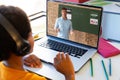 Rear view of a biracial boy having a video call with caucasian male teacher on laptop at home Royalty Free Stock Photo