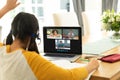 Rear view of biracial girl raising hand to ask questions during online class over laptop at home