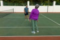 Rear view of biracial senior woman playing tennis with senior man in tennis court during sunny day Royalty Free Stock Photo
