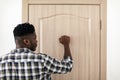 Rear View Of Black Guy Knocking At Entry Door Indoors