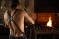 Rear view of a blacksmith in front of his newly lit forge in the workshop