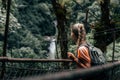 Rear view of blonde woman hiker crossing suspension bridge inside rain forest Royalty Free Stock Photo