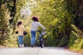 Rear View Of Boy With Bike And Girl With Skateboard Walking Along Country Road Together Royalty Free Stock Photo