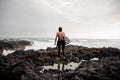 Rear view brunette boy standing in the black swimsuit with naked torso with a white surf in his hands on the shore Royalty Free Stock Photo