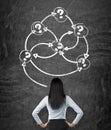 Rear view of a brunette business lady who is looking at the black chalk board with drawn arrows with question marks as a concept o