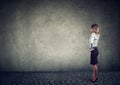 Rear view of business woman standing by the wall with hand on head wondering what to do next being challenged. Full length of