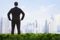 Rear view of businessman with hands on hips standing in a green field and looking at the city skyline