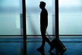 Rear view of businessman walking with bag outside airport. Young traveler pulling suitcase.