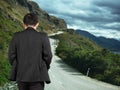Rear view businessman walking on mountain road with cloudy sky Royalty Free Stock Photo