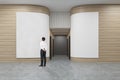 Rear view of a businessman in a white shirt looking at a poster in an office hall with rounded wooden walls.