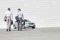 Rear view of businessmen carrying briefcases while walking towards car on street