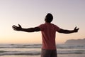 Rear view of carefree african american young man with arms outstretched standing on beach at sunset Royalty Free Stock Photo
