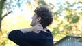 Rear view Caucasian man massaging his neck, shoulders , and back in green park. Back view sportsman with curly brown Royalty Free Stock Photo