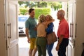 Rear view of caucasian senior couple hugging their family at entrance of house
