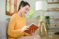 Rear view, Charming Asian woman reading a book on sofa in her living room