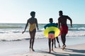 Rear view of cheerful african american parents and children with swimming floats running at seashore