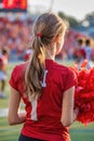 Rear view of a cheerleader with red pom-poms at a football game Royalty Free Stock Photo