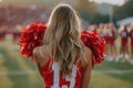 Rear view of a cheerleader with red pom-poms at a football game Royalty Free Stock Photo