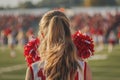 Rear view of a cheerleader with red pom-poms at a football game Royalty Free Stock Photo