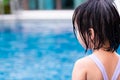 Rear view child girl wearing swimming suit in blue pool. Kid playing water in the summer time. Children safety precautions.