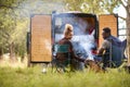 Rear View Of Couple Camping In Countryside With RV Drinking Coffee By Outdoor Fire With Pet Dog Royalty Free Stock Photo