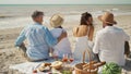 Rear view of couple friends at beach having picnic celebration with wine and tasty meal.