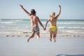 Rear view of couple holding hands while jumping at beach Royalty Free Stock Photo