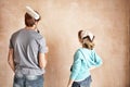 Rear view of couple with paint roller looking at wall in unrenovated room Royalty Free Stock Photo
