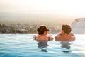 Rear view of couple relaxing at luxury resort on outdoor pool. Romantic summer vacation. People in edge swimming pool Royalty Free Stock Photo