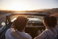 Rear View Of Couple On Road Trip Driving Classic Convertible Car Towards Sunset Royalty Free Stock Photo