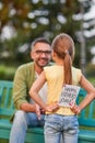 Rear view of cute little girl hiding handmade postcard Happy Fathers Day behind her back while greeting her dad