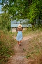 Rear view of a cute little girl walking along a small farm path in the countryside to a traditional wooden house painted blue