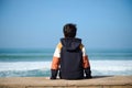 Rear view of teenage hipster boy sitting on the edge of Atlantic Ocean, enjoying the view of waves pounding on the shore