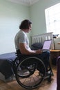 Rear view of disabled man sitting on wheelchair using laptop with copy space on couch at home Royalty Free Stock Photo