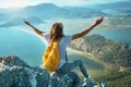 Faceless tourist girl sits on rock with arms up, enjoying amazing scenic nature view over sea coast