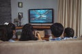 Rear view of family sitting at home together watching swimming competition on tv