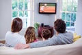 Rear view of family sitting at home together watching tennis match on tv