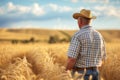 Rear view of a farmer in a straw hat standing in a wheat field, with a vast expanse of golden crops extending to the