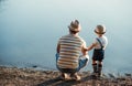 A rear view of father with a small toddler son spending time outdoors by a lake.