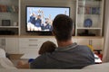 Rear view of father and son sitting at home together watching football match on tv Royalty Free Stock Photo