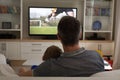 Rear view of father and son sitting at home together watching football match on tv Royalty Free Stock Photo