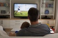 Rear view of father and son sitting at home together watching football match on tv Royalty Free Stock Photo